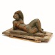 Skulptur i form af liggende kvinde udført i brun- og grønglaseret lertøj. Mål inkl. originalt træpodie: H: 35cm. L: 65cm. B: 31cm